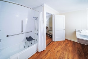 Une salle de bain moderne dotée d’une douche à l’italienne, de barres d’appui, d’un banc accessible aux personnes en fauteuil roulant et d’un plancher en bois.
