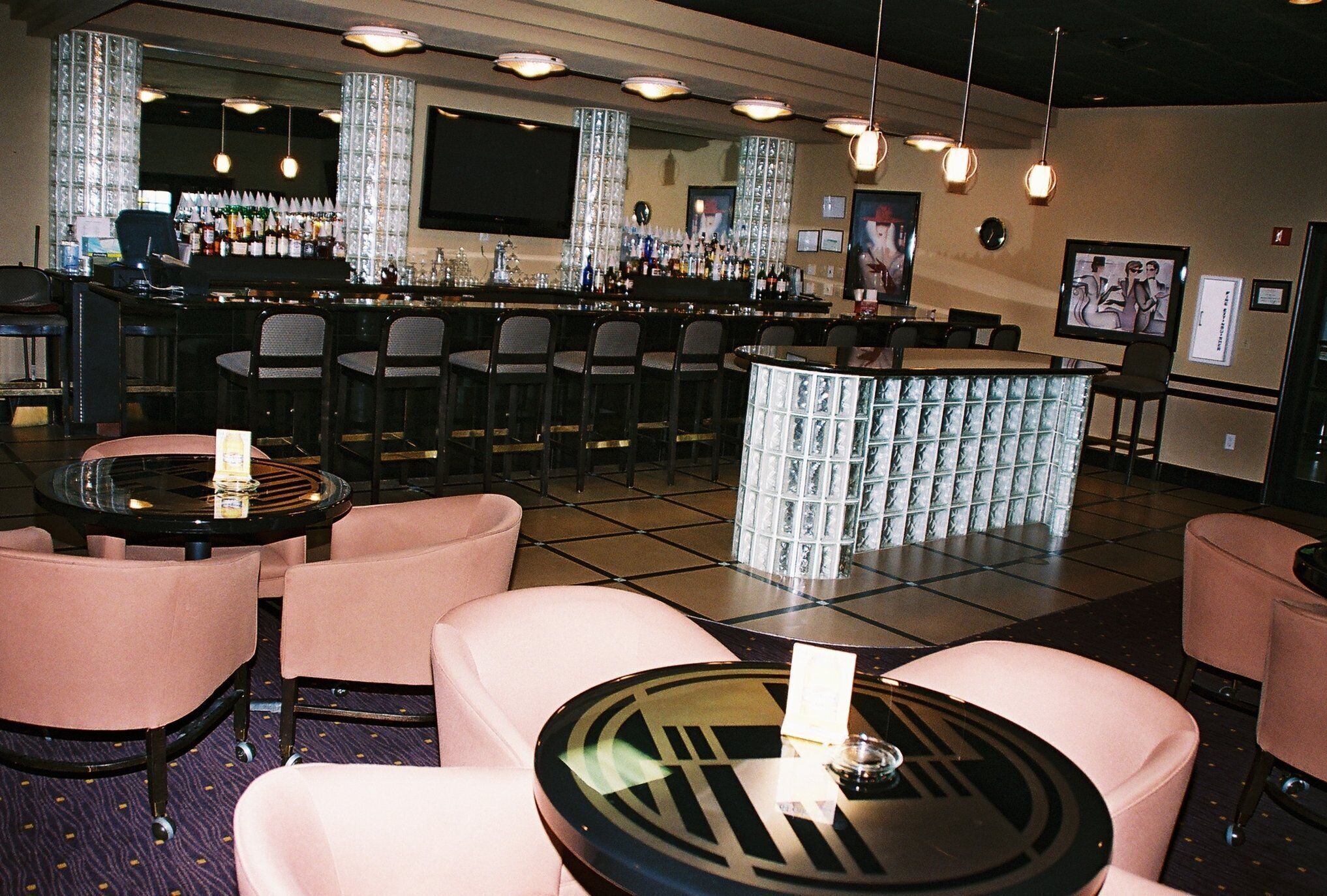 A bar area with multiple seating options, including round tables and bar stools, and a bar counter with various bottles and glasses.