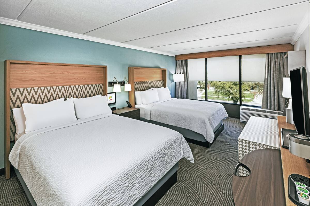 A hotel room with two beds, a desk, a TV, and a large window with a view.