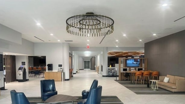 Un vestíbulo amplio con una lámpara moderna, zona de estar con sofás y sillones, mostrador de recepción y una pantalla de televisión.