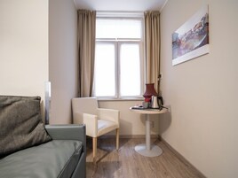 Une pièce comprenant un canapé, un fauteuil, une petite table avec une lampe, une cafetière et un tableau accroché au mur.