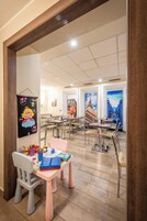 A children's play area with a table and chairs, a wall with a cartoon character, and a large window with a view of buildings.