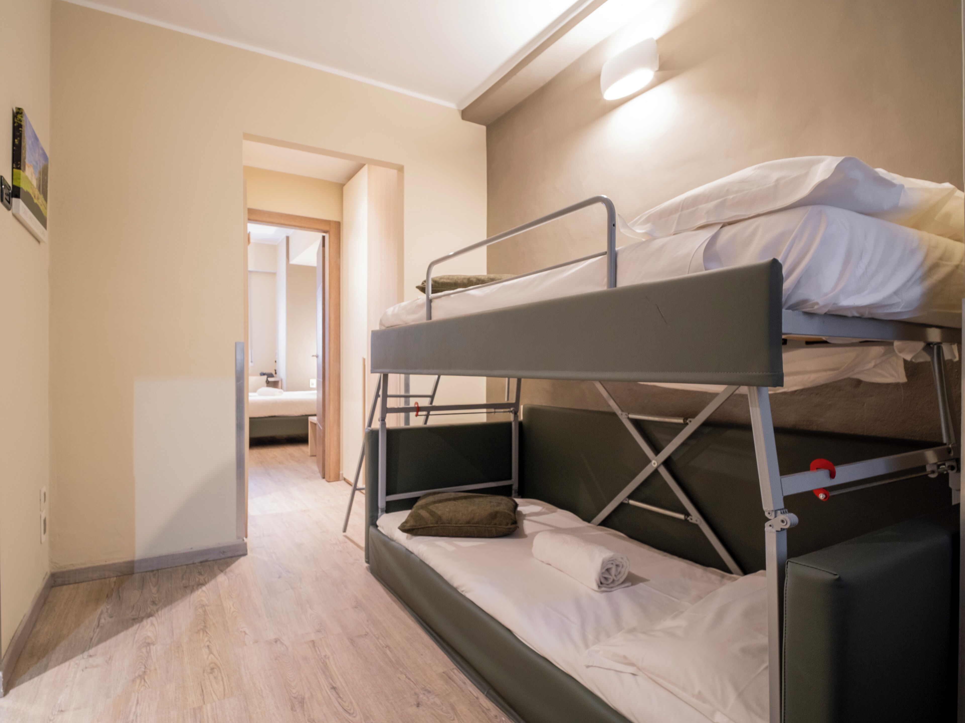 A bunk bed room with a wooden floor, a small desk, and a door leading to another room.
