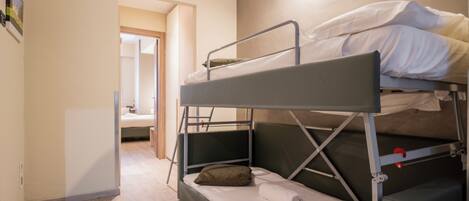 A bunk bed room with a wooden floor, a small desk, and a door leading to another room.