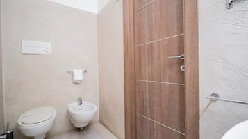 A modern bathroom with a wooden door, a toilet, and a bidet.