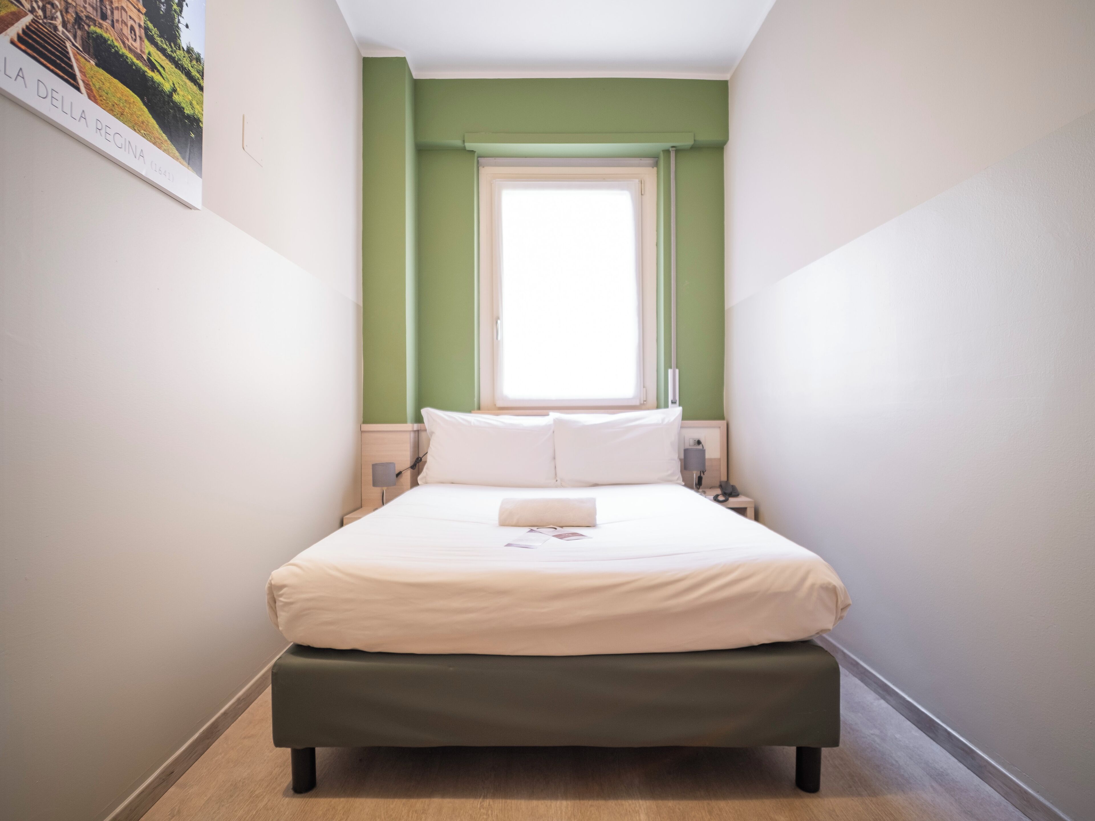 Une chambre à coucher avec un lit, une fenêtre, une table de chevet et une lampe fixée au mur.