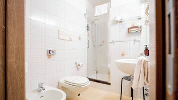 A modern bathroom with a toilet, bidet, sink, and glass shower enclosure.