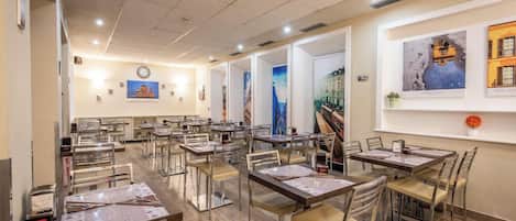 A restaurant with multiple tables and chairs, a clock on the wall, and framed artwork on the walls.