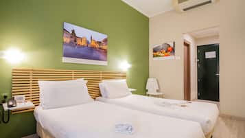 Quarto de hotel com duas camas, uma parede verde e uma imagem da paisagem urbana.