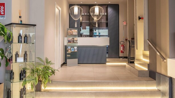 A modern reception area with a glass display case, a reception desk, and a staircase leading to upper floors. - Best Quality Hotel Gran Mogol (Turin)