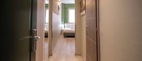 A hallway with a bed at the end, a door on the left, and a mirror on the wall.