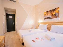 Une chambre d’hôtel avec deux lits, une tête de lit en bois, un tableau accroché au mur et une porte avec une pancarte.