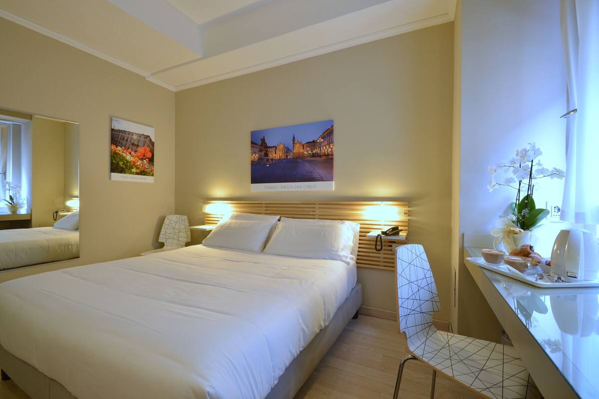 Une chambre d’hôtel avec un grand lit, un bureau avec une chaise, une table de chevet et deux tableaux encadrés au mur.