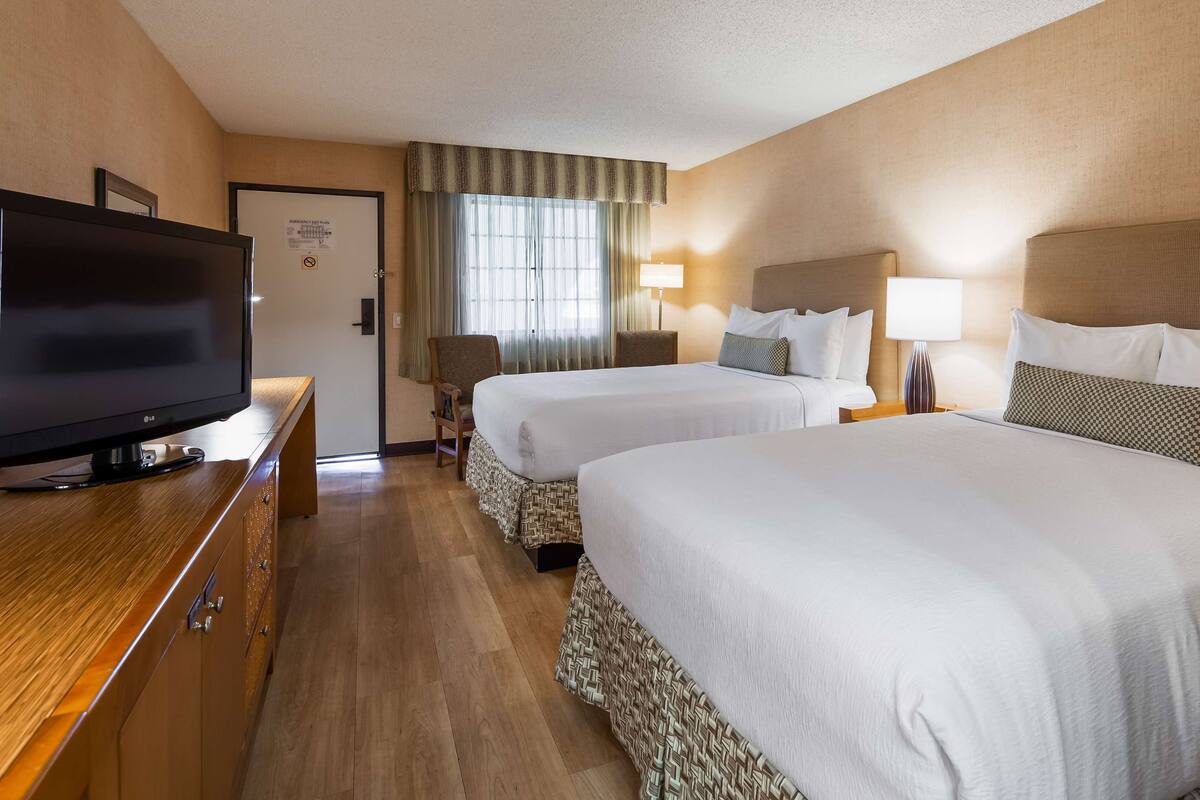 Ein Hotelzimmer mit zwei Betten, einem Fernseher, einem Schreibtisch und einem Fenster mit Vorhängen.