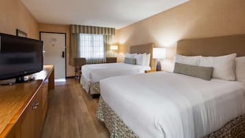 Una habitación de hotel con dos camas, televisión, escritorio y ventana con cortinas.
