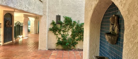 Un patio con baldosas de terracota, un muro cubierto de plantas verdes y una fuente de piedra.