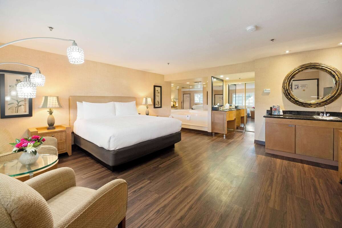 Ein Hotelzimmer mit einem großen Bett, einem Glastisch mit Stühlen, einem Schminktisch mit Spiegel und einer Küchenzeile.