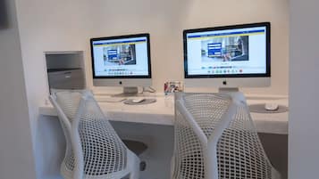Dois computadores Apple iMac sobre uma mesa branca com cadeiras de tela.