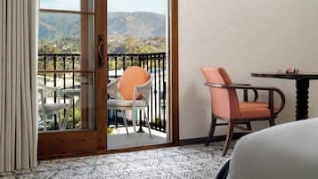 Une chambre avec un balcon, une chaise, une table et une vue sur les montagnes.