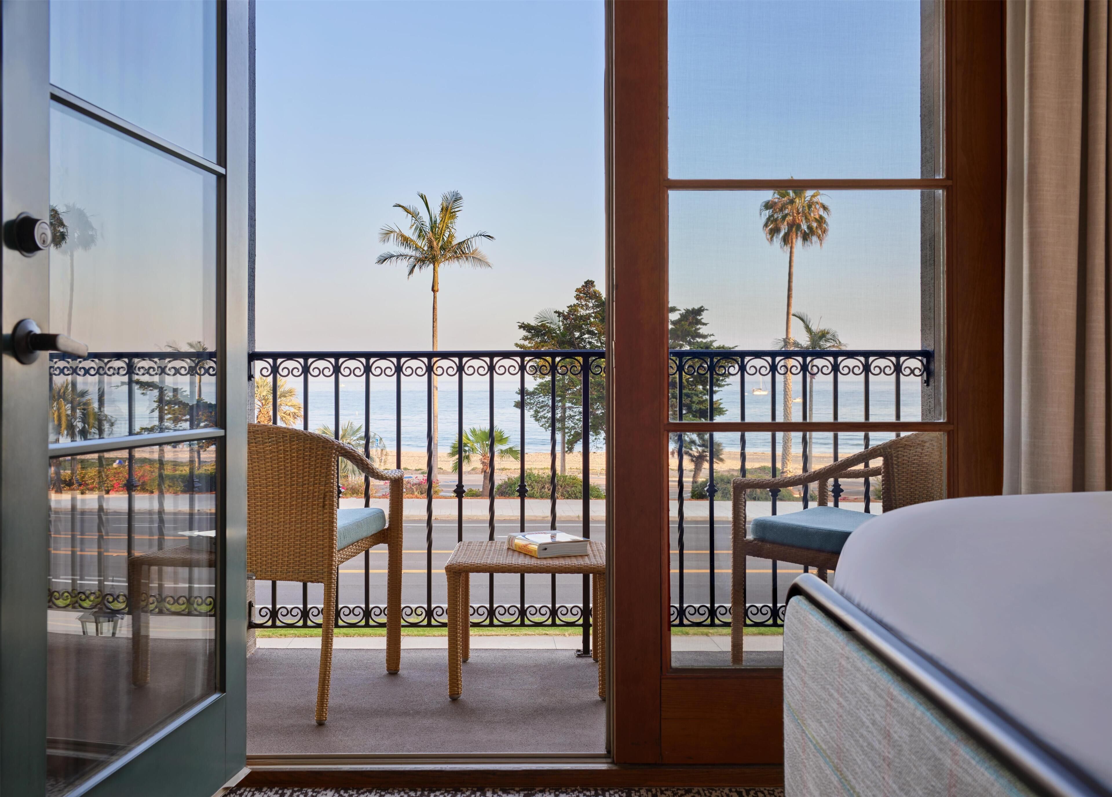 A balcony with wicker furniture, a small table, and a view of the beach and palm trees.