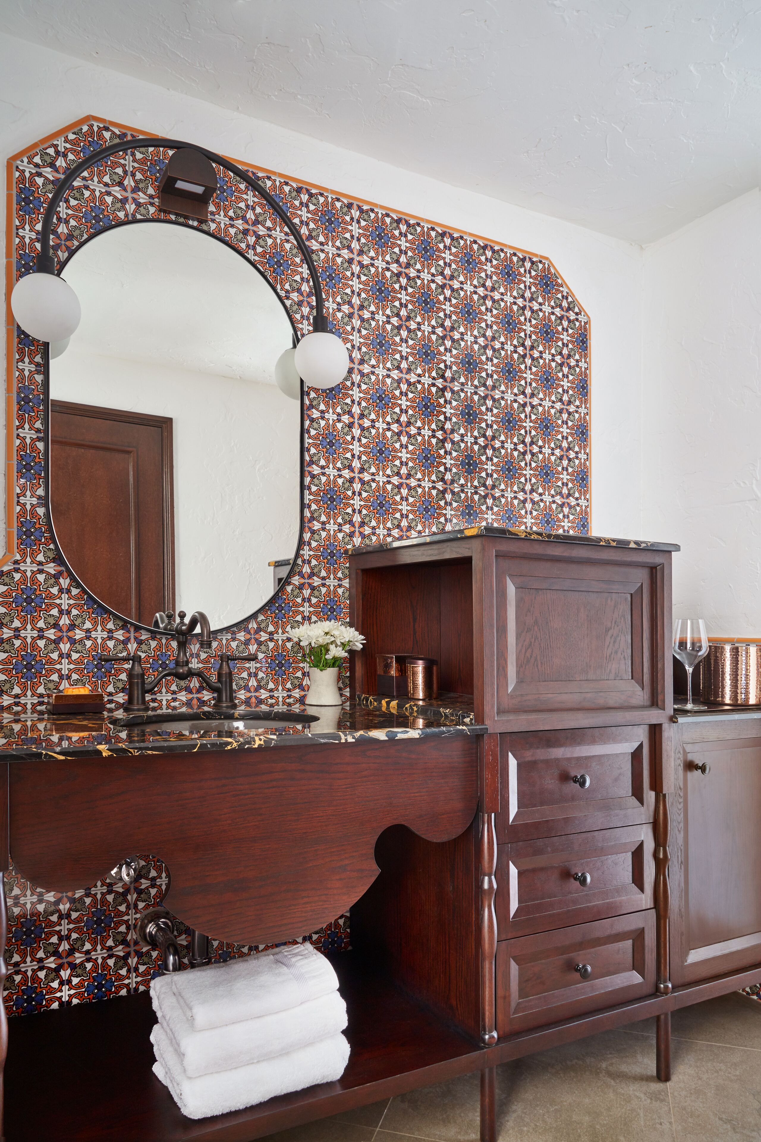 Un baño con tocador de madera, un espejo grande y un revestimiento de azulejos estampados.