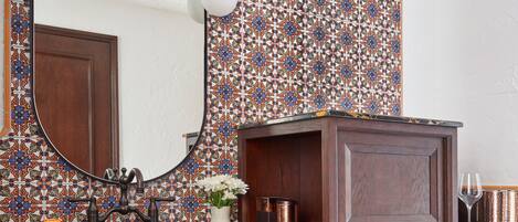 Un baño con tocador de madera, un espejo grande y un revestimiento de azulejos estampados.