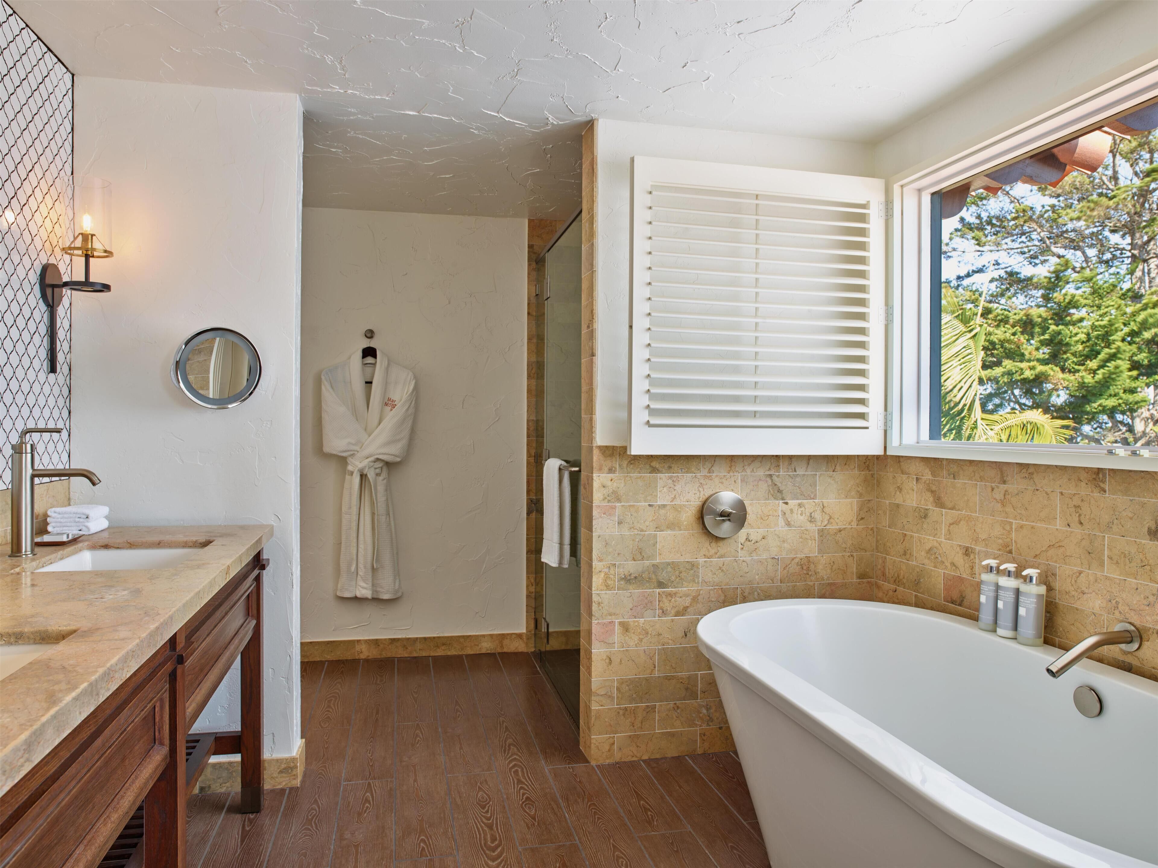 Un baño con bañera, lavamanos, espejo y ventana con persianas.