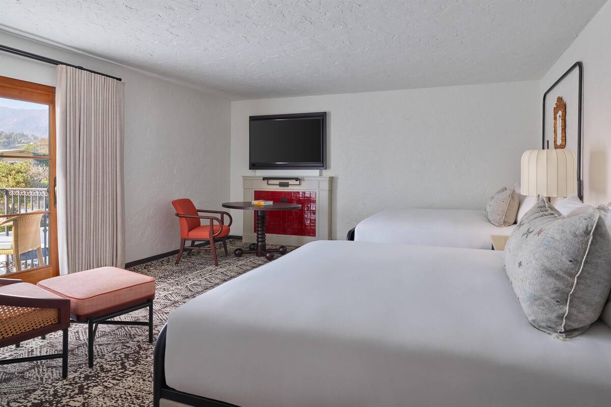 A hotel room with a bed, a desk, a chair, a TV, and a view of the outdoors.