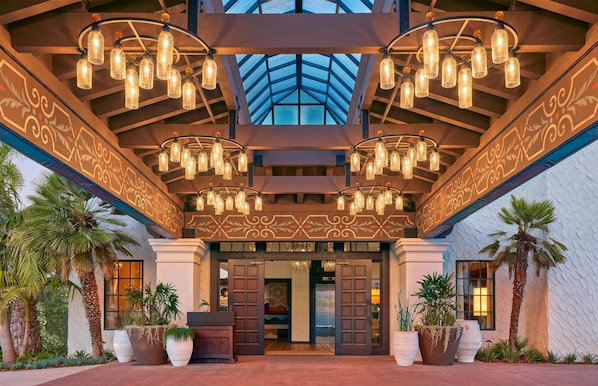 Ein Hotel Eingang mit hoher Glasdecke, mehreren Kronleuchtern und Palmen.