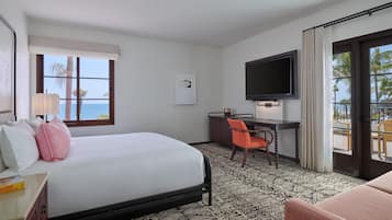 A hotel room with a bed, desk, chair, TV, and a view of the ocean.