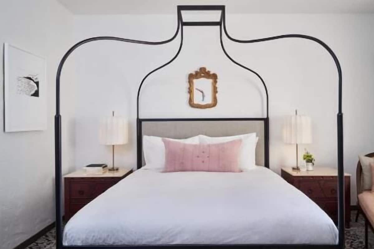 A bed with a unique headboard design, two bedside tables with lamps, and a small framed mirror.
