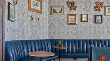A blue leather booth with a round wooden table, framed pictures on the wall, and a patterned wallpaper.