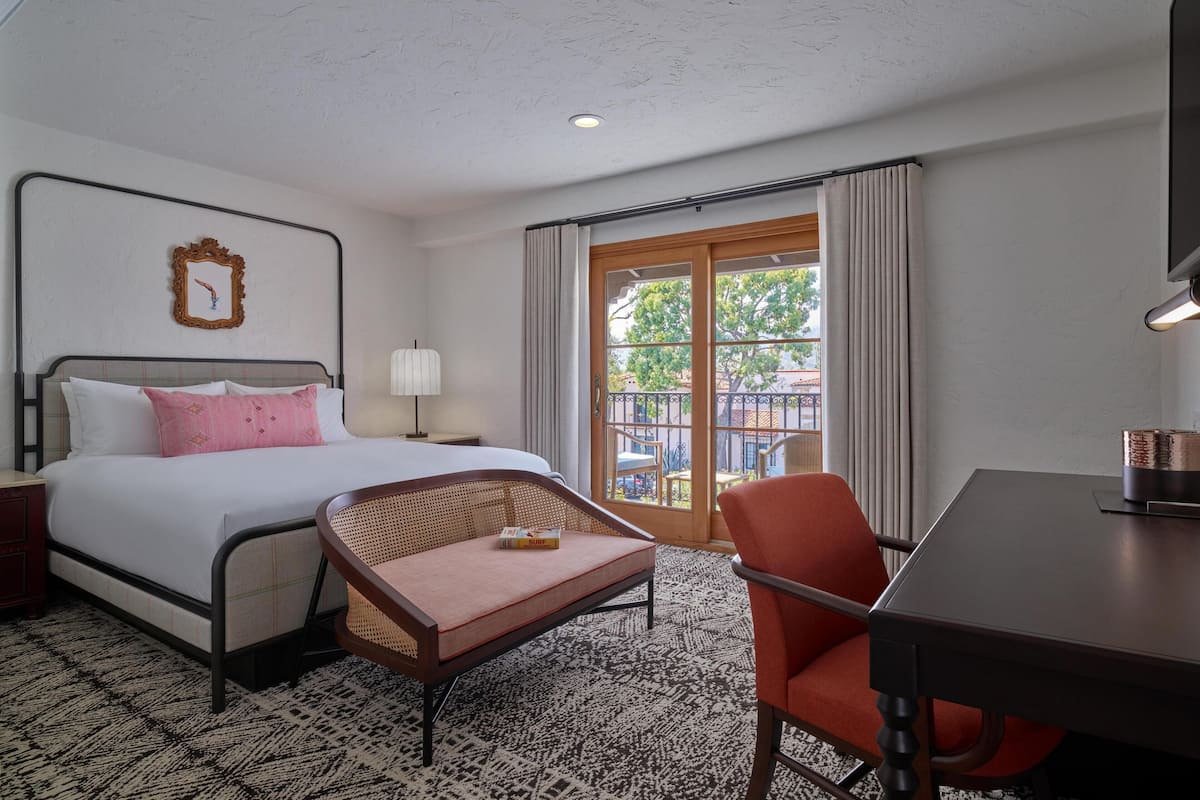 A hotel room with a bed, a small table, a chair, a window with curtains, and a view of the outside.