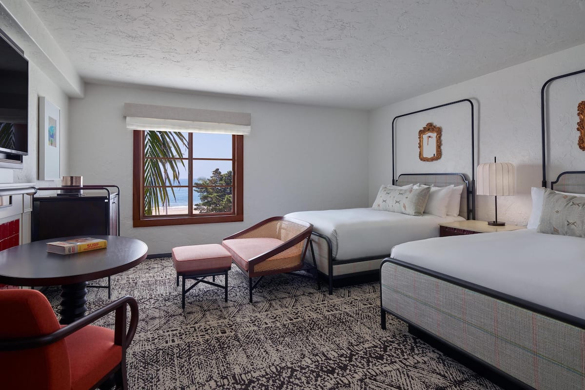 A hotel room with two beds, a dining table, a chair, a window with a view, and a television.