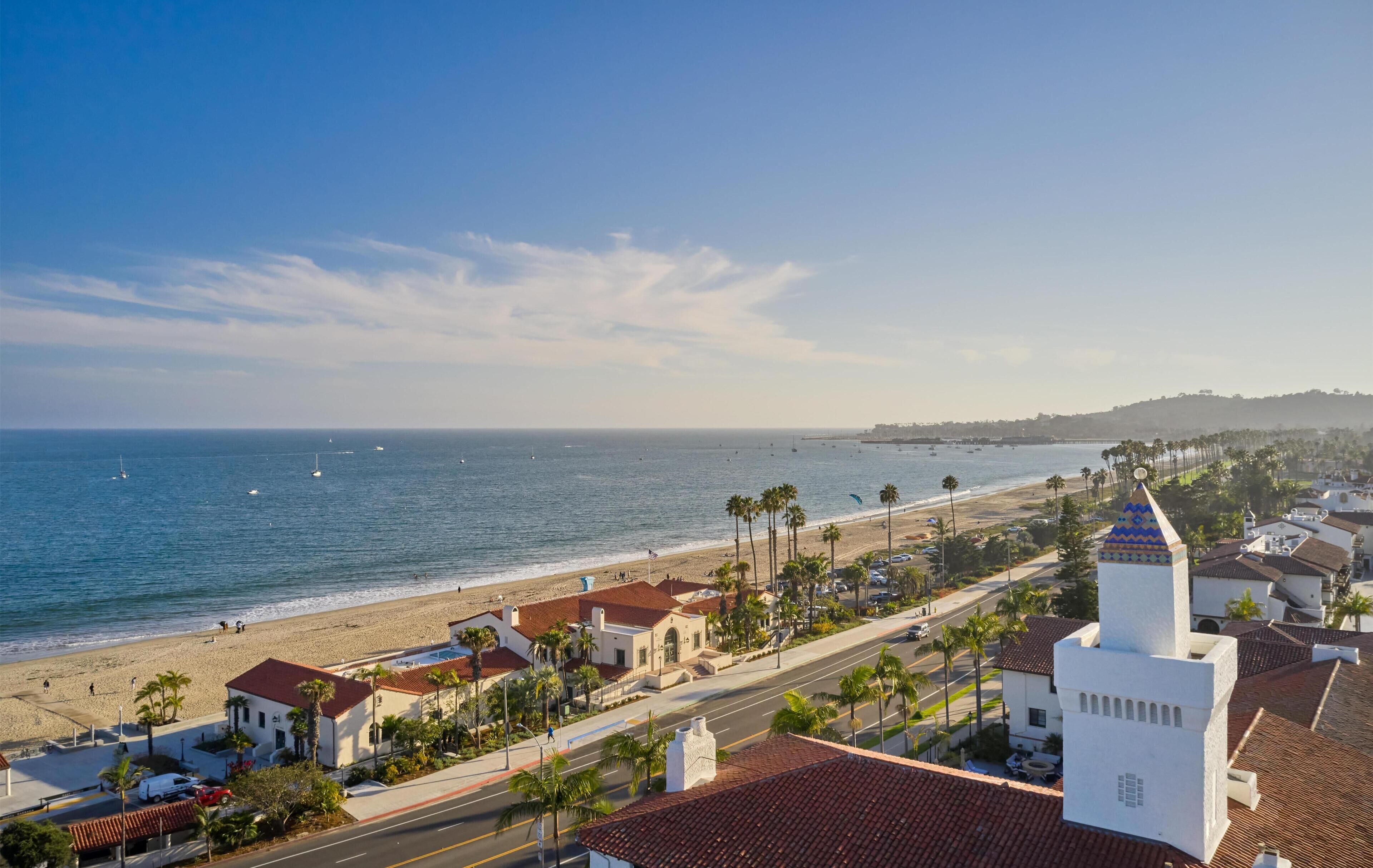 Un pueblo costero con playa, palmeras y un edificio blanco destacado con una torre.