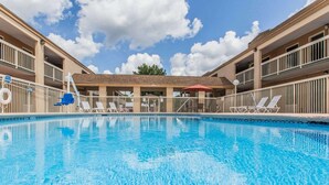 Una piscina con sillas de descanso y sombrillas, rodeada por un edificio con balcones.
