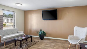 Una sala de estar con un sofá, una mesa de centro, un televisor montado en la pared, una planta en maceta y una silla.
