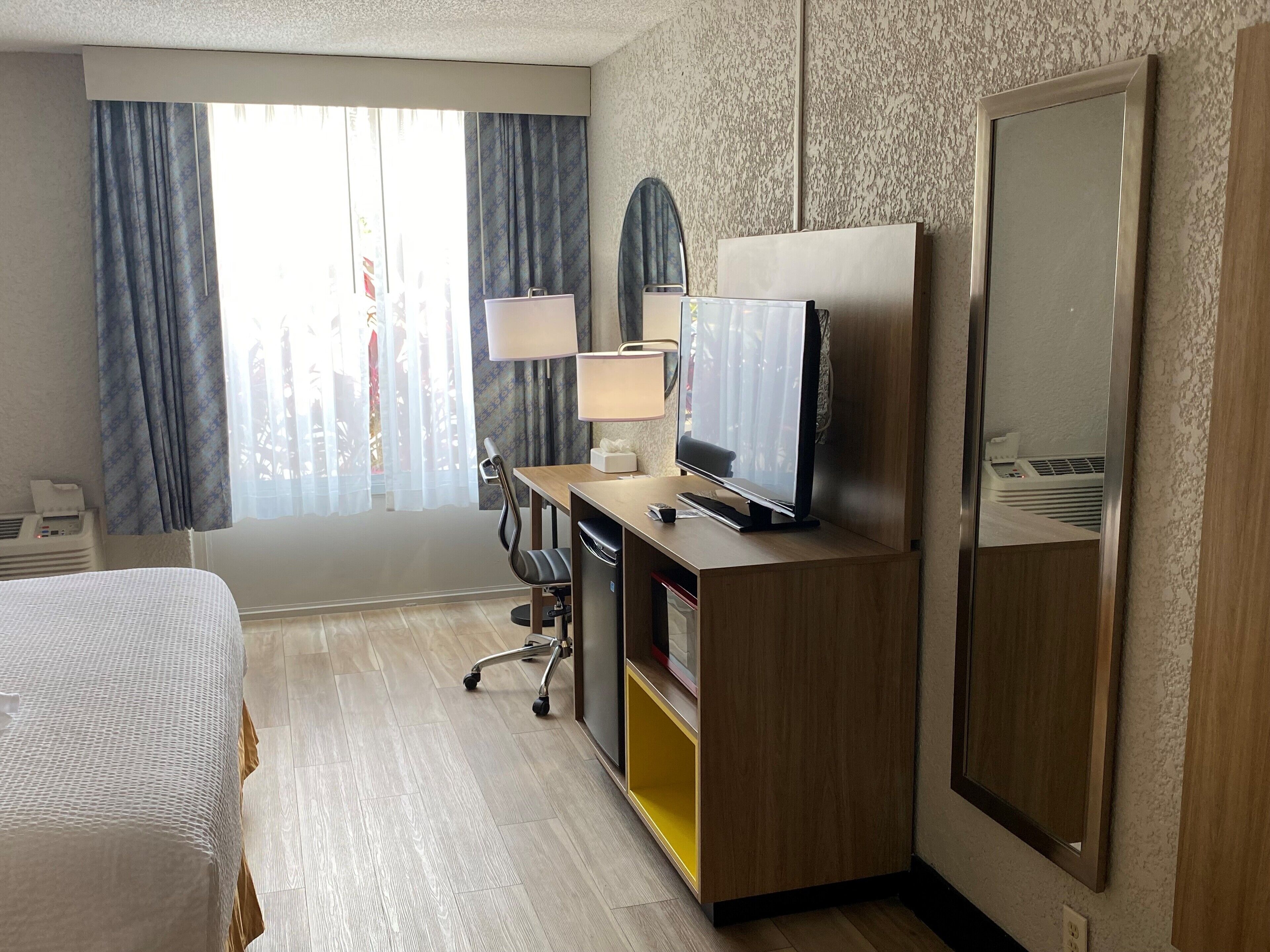 A hotel room with a bed, desk, TV, and wardrobe.