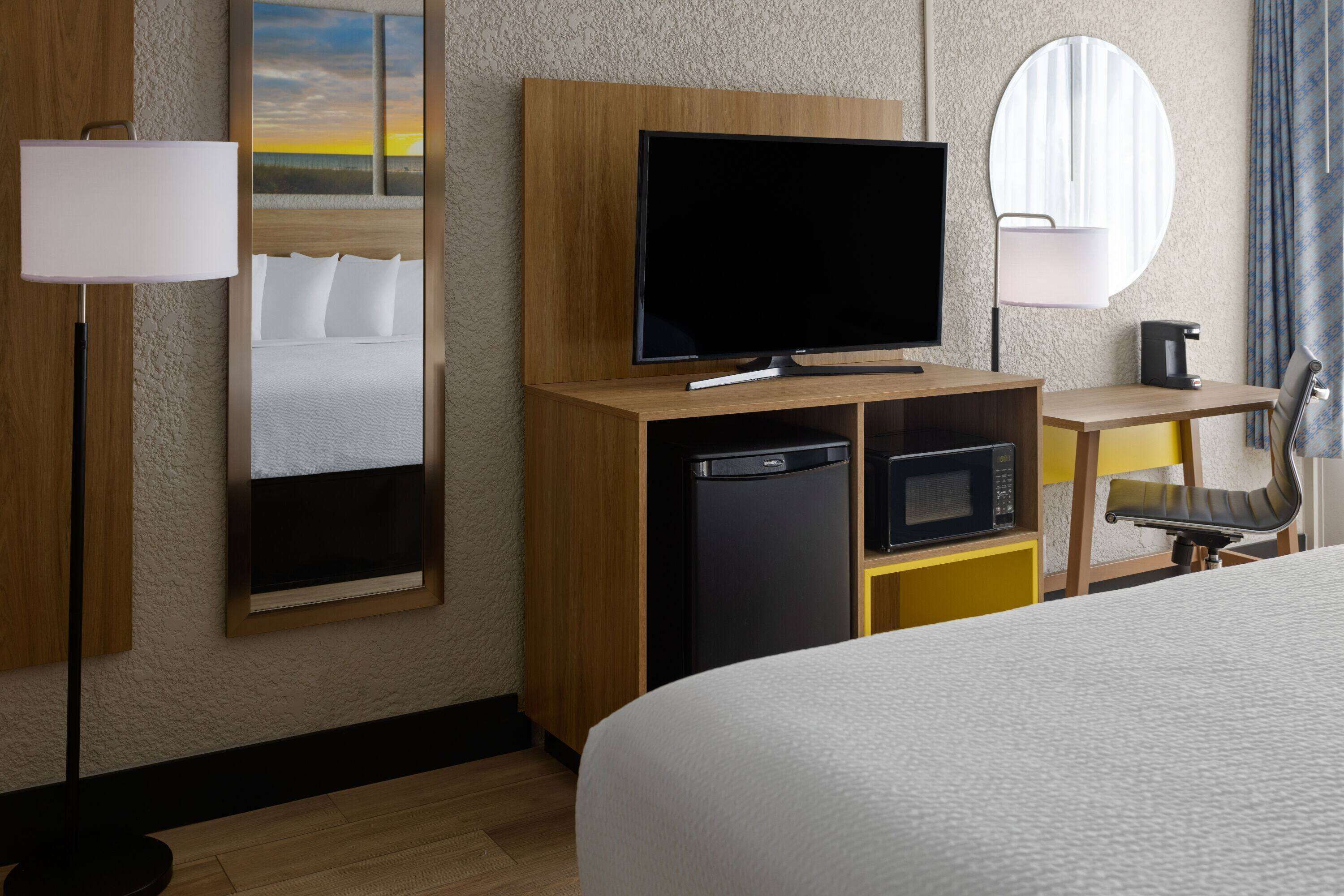 A hotel room with a bed, a flat-screen TV, a microwave, a coffee maker, and a desk with a chair.