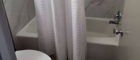 A bathroom with a bathtub, toilet, and marble walls.