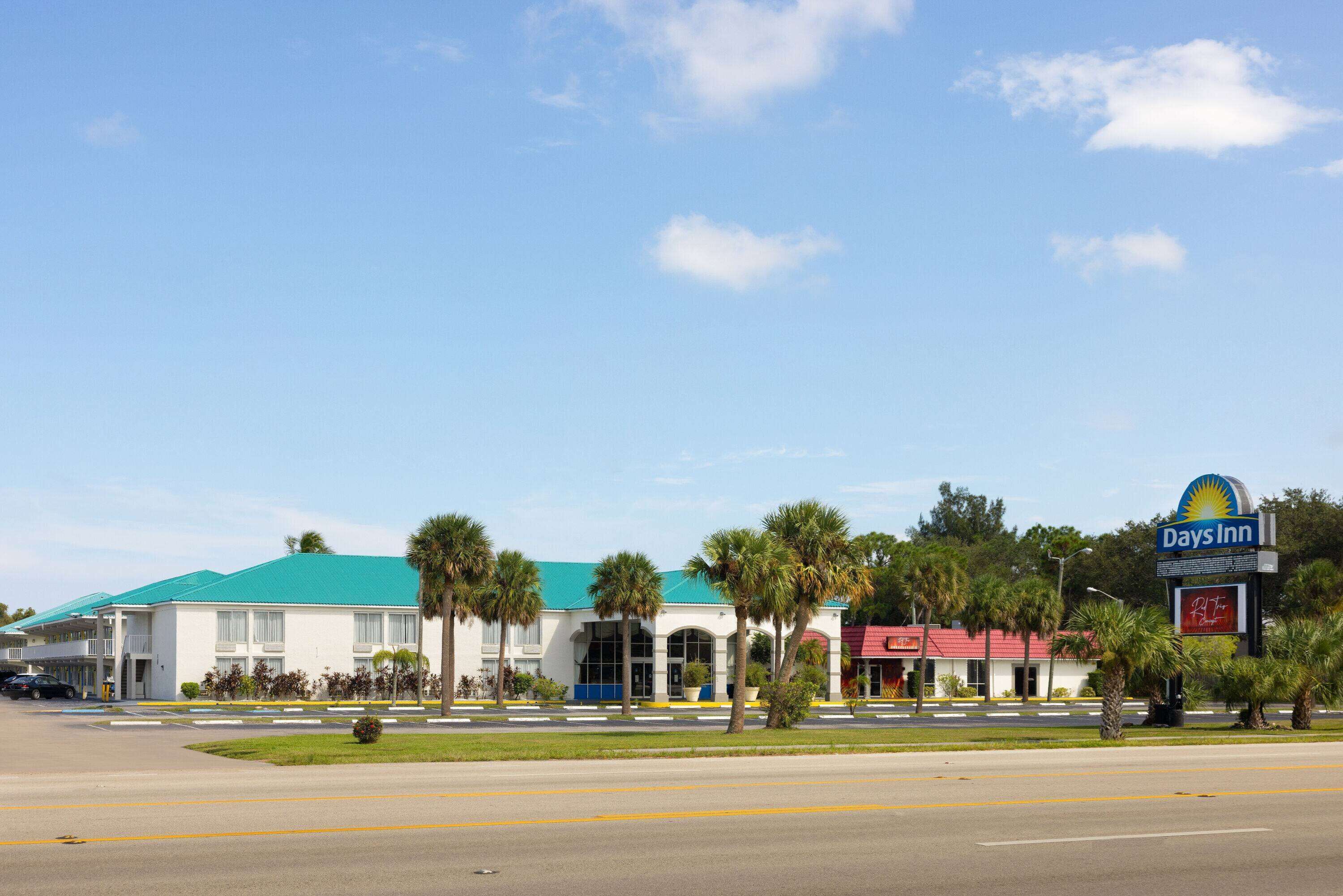 A Days Inn with a green roof, palm trees, and a red building across the street.