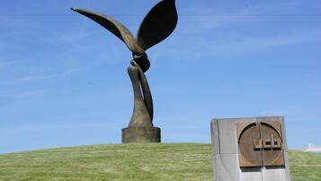 Una escultura de un ave con alas extendidas sobre una colina cubierta de hierba, junto a una placa de metal con las letras "UCB".