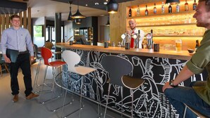A modern bar area with a bar counter, stools, and a variety of bottles and glasses. - ibis Brussels Erasmus (Brussels)