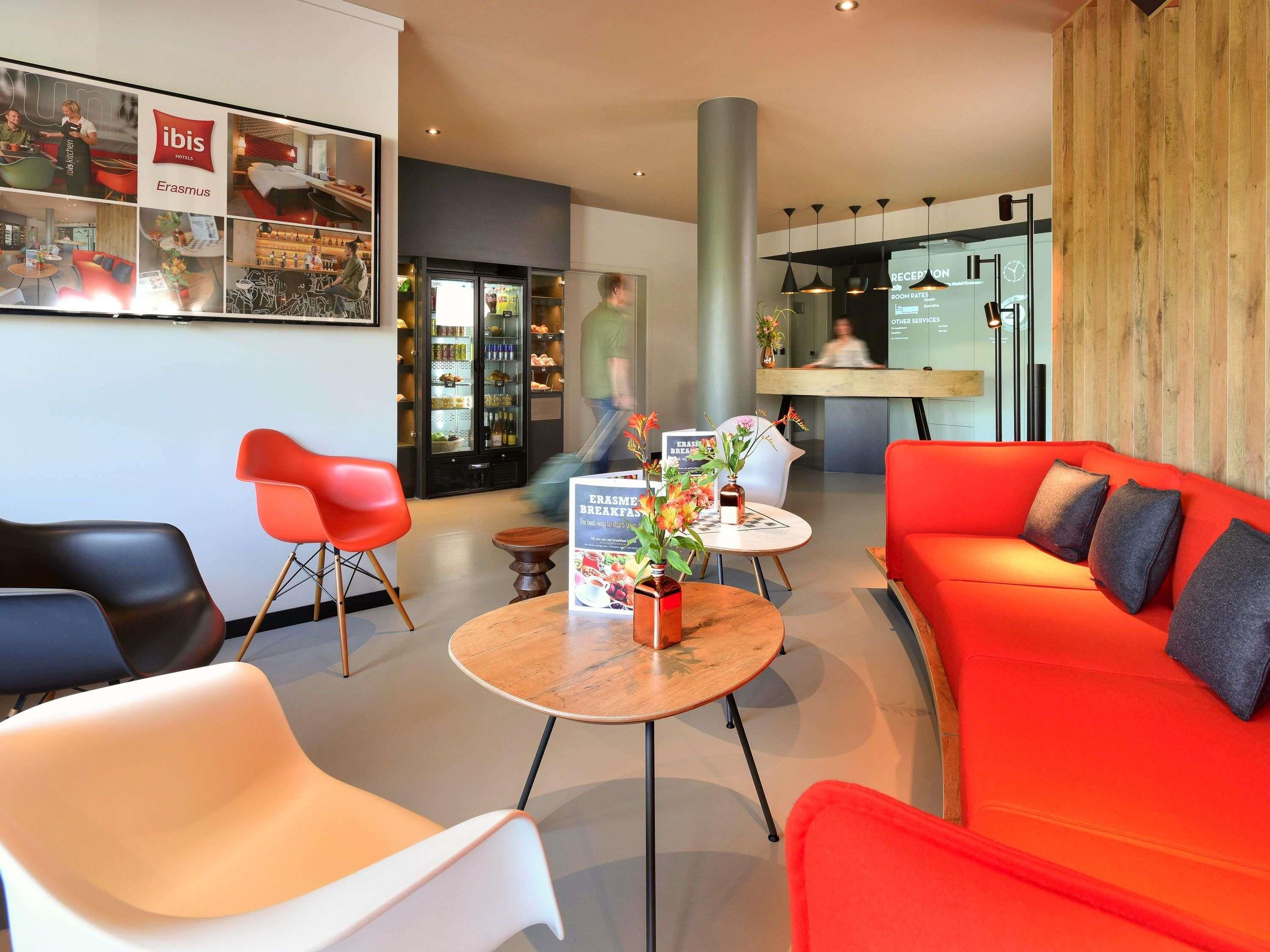 Un vestíbulo de hotel con mostrador de recepción, un sofá rojo y una mesa de centro con un cartel sobre el desayuno.