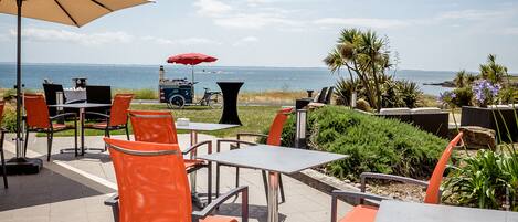 Un espace extérieur aménagé avec des tables et des chaises, offrant une vue sur la mer.