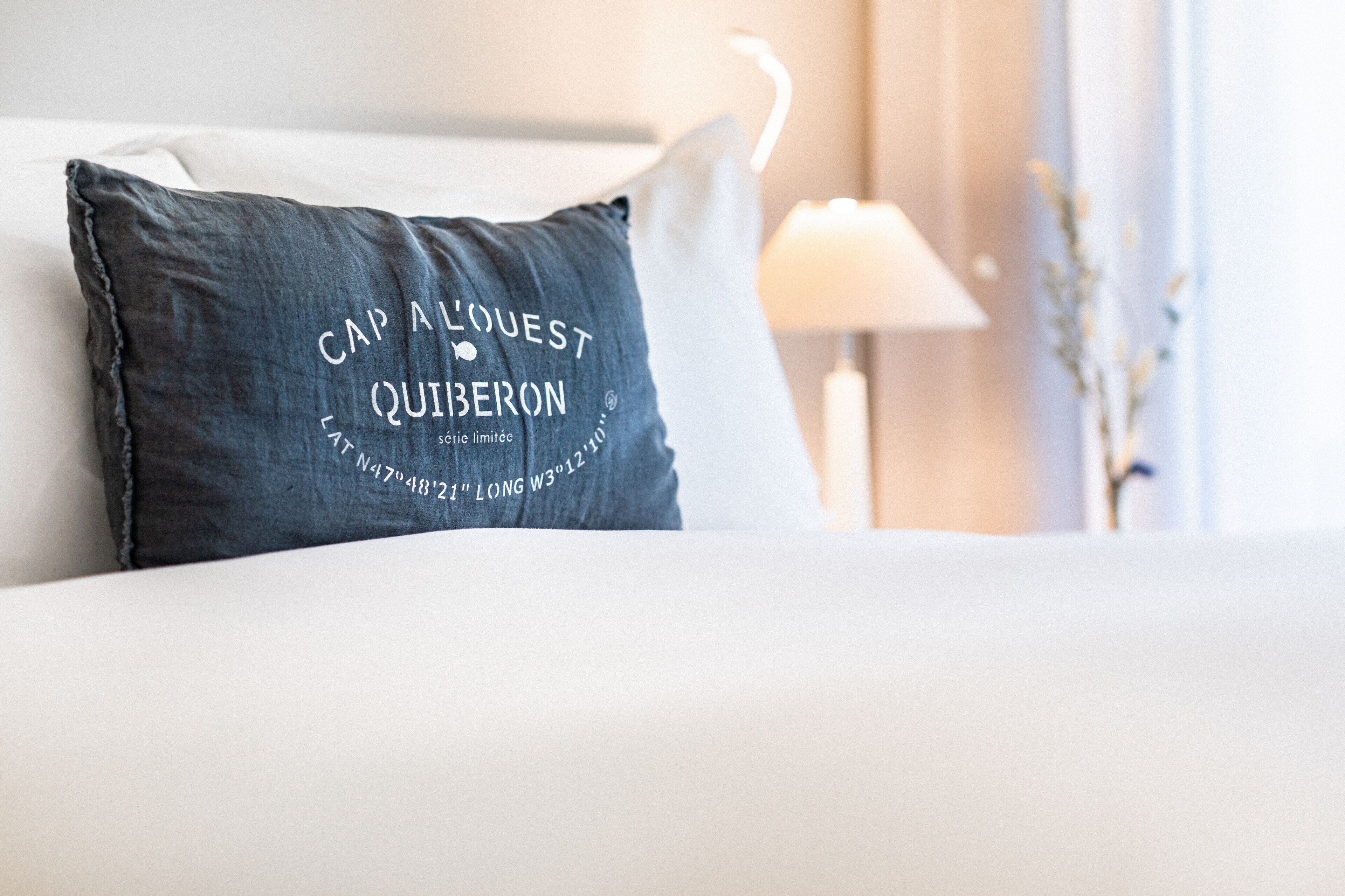 A bed with a pillow featuring text and a lamp in the background.