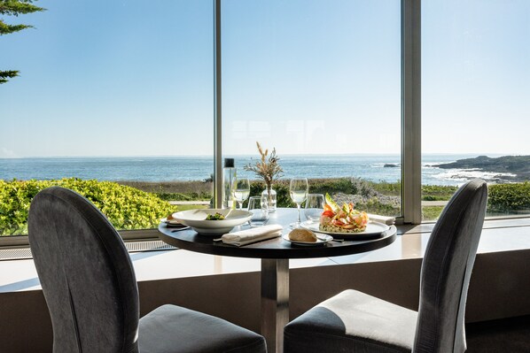 A dining table with a view of the ocean, a salad, and a glass of wine.