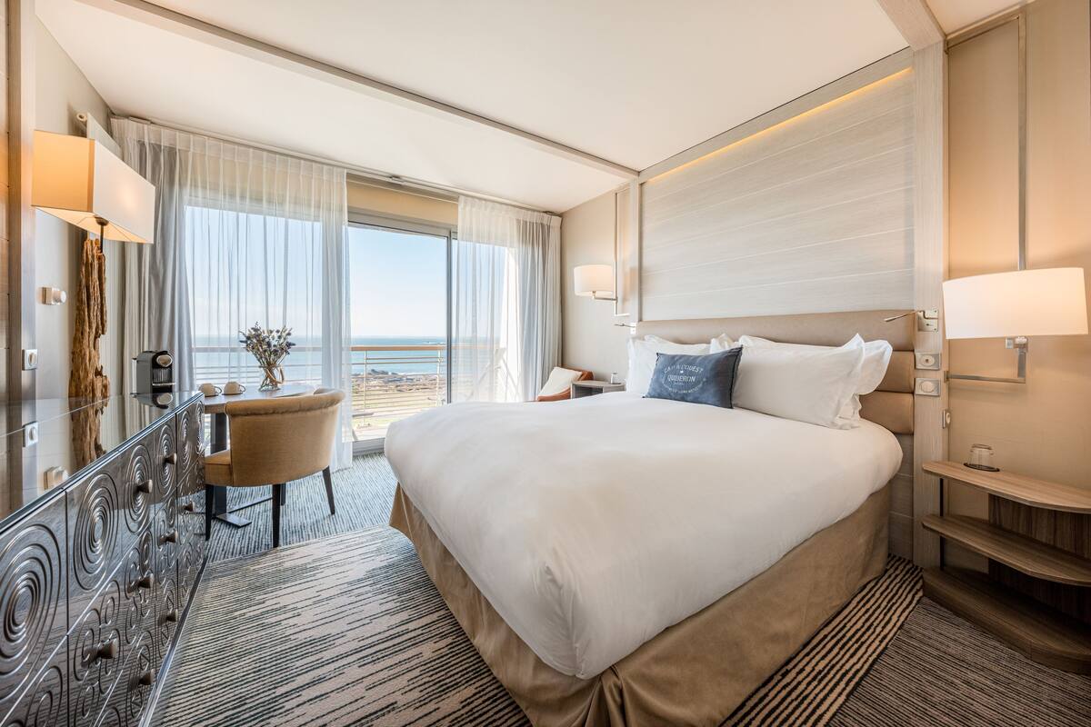 Ein Hotelzimmer mit einem großen Bett, einem Schreibtisch und Meerblick.