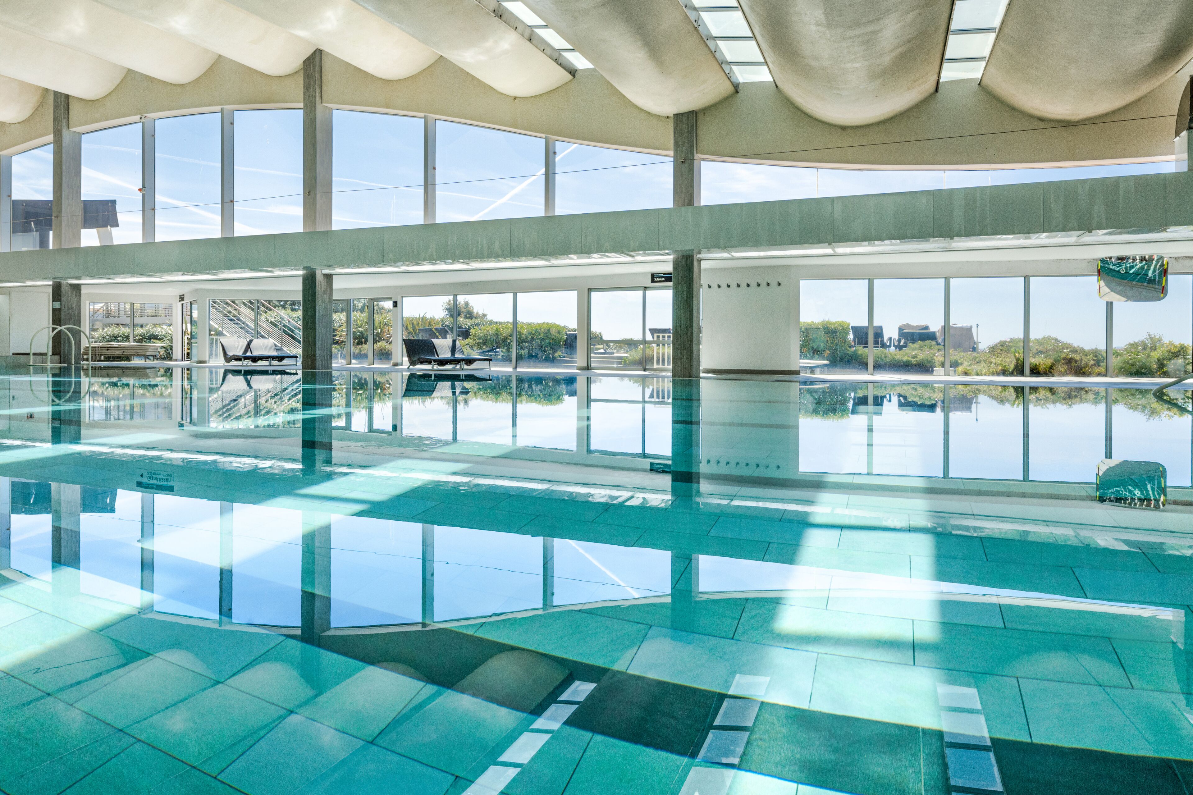 A large indoor swimming pool with clear glass walls, a sunroof, and a view of the surrounding landscape.