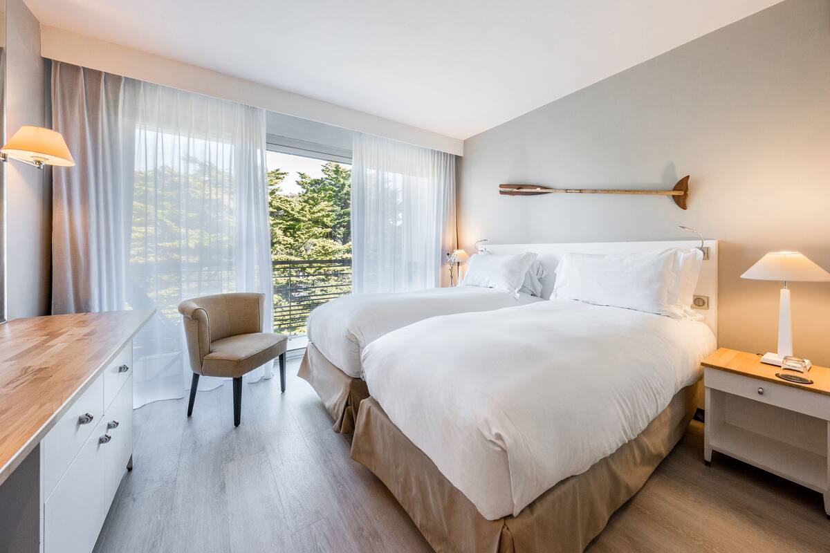 Ein Hotelzimmer mit zwei Betten, einem Schreibtisch, einem Sessel und einem Nachttisch mit Lampe.